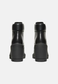Botas de cuero negras hasta el tobillo con un tacón grueso, que presentan una textura suave y un diseño sobrio, vistas desde atrás.