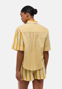 Chemise à manches courtes rayée jaune et blanche, avec un col, un dos plissé et une coupe décontractée. Associée à un short assorti à rayures.