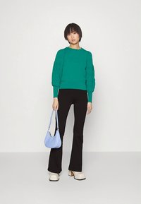 Zaļš džemperis ar faktūrām uzpūstām piedurknēm, kombinēts ar melnām stieptām biksēm. Aksesuāri: neliela gaiši zila soma un krēmkrāsas platformas apavi.