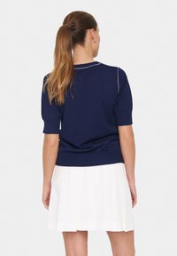 Pull en maille bleu marine à manches courtes, au design ajusté, avec un col côtelé. Associé à une jupe plissée blanche.