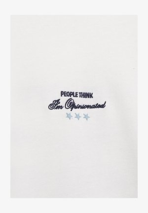 Bílá látka s černým vyšitým nápisem „Lidé si myslí, že mám silné názory“ nad třemi světle modrými hvězdami.