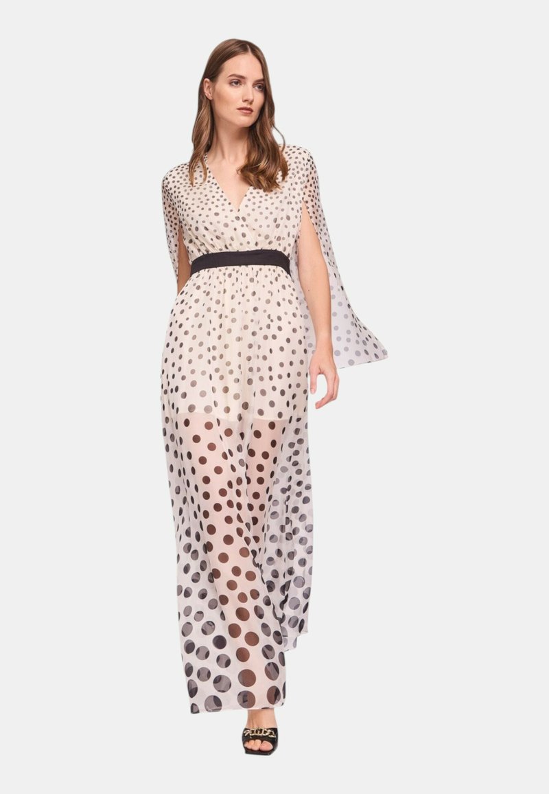 Abito lungo e trasparente con motivo a pois nero e beige, caratterizzato da scollatura a V, maniche corte a mantella e una cintura nera in vita.