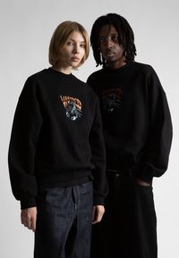 Felpe nere dal taglio rilassato con una grafica a scorpione multicolore sul petto. Tessuto caldo con polsini e orlo a costine.