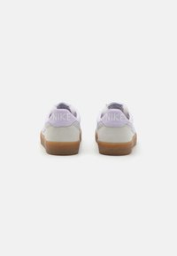 Adidași Nike de culoare violet și gri deschis cu talpă din cauciuc de tip gumă. Prezintă un spate texturat și un branding proeminent "NIKE" în alb.