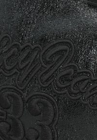 Materiale in pelle nera con testo ricamato in rilievo in un font sinuoso, dalla texture liscia e lucida con motivi delicati.