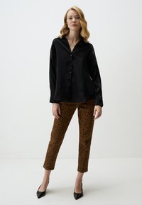 Black satin button-up shirt with a collar, paired with brown leopard print fitted trousers, and black pointed toe heels. Simple background.