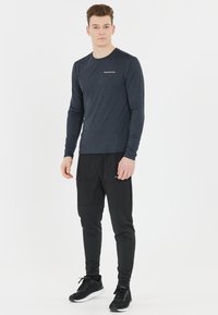 Maglietta atletica a maniche lunghe, blu navy, realizzata in tessuto leggero e traspirante; abbinata a pantaloni jogger neri con tasche e gambe affusolate.