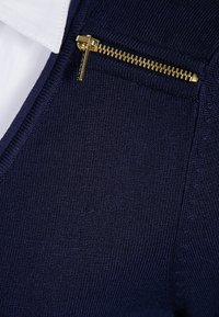 Navy knitted pullover featuring a V-neck, with a textured fabric, and a gold zipper pocket detail on the chest.