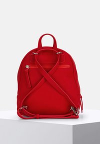 Zaino rosso con forma arrotondata, realizzato in materiale morbido. Presenta spallacci incrociati, una tasca frontale con zip e accessori in argento.