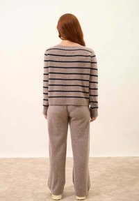 Szary sweter w paski z granatowymi paskami, z dzianinowymi mankietami, okrągłym dekoltem; zestawiony z dopasowanymi, miękkimi, szarymi spodniami o szerokim kroju. Widok z tyłu.