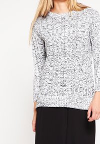 Grau-weißes Strickpullover mit strukturiertem Muster, langen Ärmeln und Rundhalsausschnitt. Der Saum und die Bündchen sind gerippt.