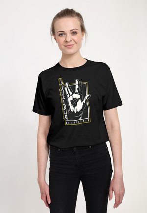 Lachende vrouw draagt een zwart T-shirt met een witte hand die de Vulcaanse groet maakt en de tekst "Live Long and Prosper" op een witte achtergrond.