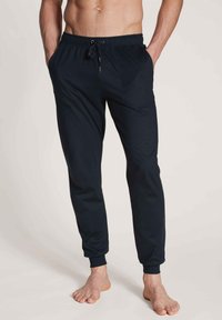 Zwarte joggingbroek van zacht materiaal met een elastische tailleband en trekkoord. Kenmerkt zich door cuffs op de enkels en zijzakken voor extra gemak.