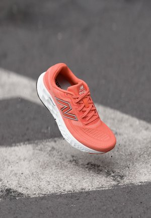 Chaussure de course corail avec tige en mesh, semelle blanche et détails texturés. Présente un logo de marque et des lacets plats pour un maintien sûr.