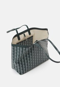 Grande borsa tote con motivo geometrico teal scuro, texture liscia, doppie maniglie e un interno beige dotato di una piccola tasca con zip.