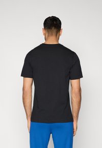 Μαύρο βαμβακερό t-shirt με στρογγυλή λαιμόκοψη, κοντά μανίκια και ίσια ρεβέρ, που φαίνεται από πίσω. Απλός σχεδιασμός, χωρίς ορατά σχέδια.