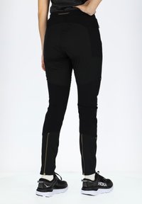 Black athletic pants with a fitted design, featuring gold zippers at the ankles and a logo at the waist. Material appears stretchy and durable.