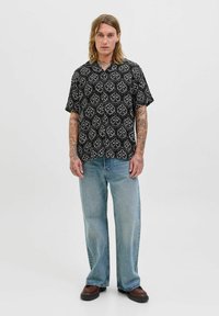 Kortærmet sort skjorte med hvidt blomsterdesign, parret med lyseblå brede jeans og mørkebrune sko, båret af en model.