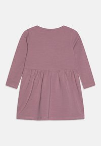 Ilga rankovė suknelė iš minkštos mauve spalvos medžiagos, su prigludusia liemene ir surinkta plačia sijonu. Lygus tekstūra su paprastais siuvinėjimo elementais.