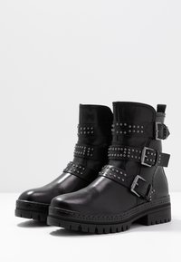 Zwarte leren enkellaarsjes met meerdere gespen en studded versieringen, voorzien van een stevige profielzool en een ronde neus.