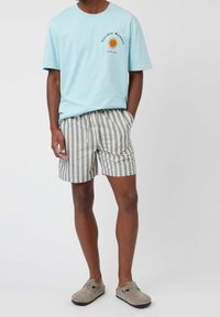 Camiseta de algodón azul claro con un gráfico del sol, combinada con pantalones cortos a rayas grises y blancos. Con un ajuste cómodo, estilo casual y calzado en tonos neutros.