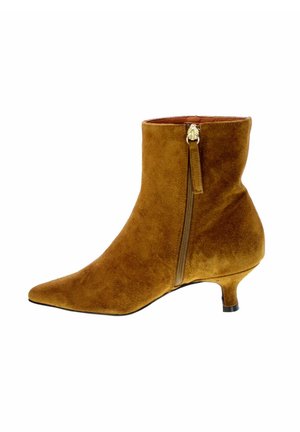 Stivaletto in suede di un caldo marrone con punta affusolata, cerniera laterale e sottile tacco kitten. Texture morbida e silhouette elegante.