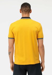 Geel polo shirt met een zwarte kraag en blauwe en witte strepen. Korte mouwen, een gladde textuur en zijsplitten aan de zoom.