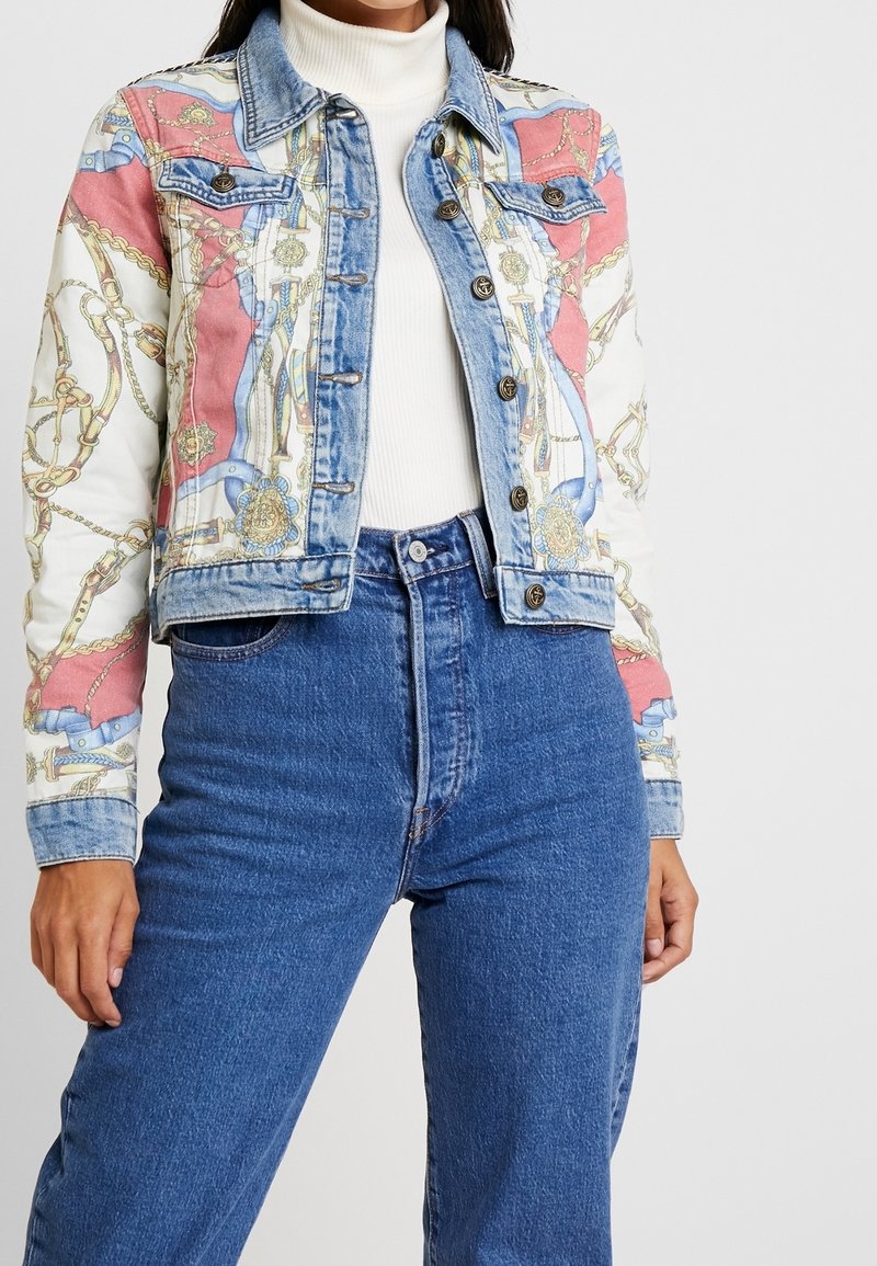 Veste en denim avec un tissu à motifs colorés, des chaînes, des accents dorés et une coupe ajustée. Manches longues avec des poignets contrastés.