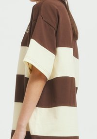 Brun och beige randig oversized T-shirt i bomull med korta ärmar, som har en avslappnad passform och synliga sömdetaljer.