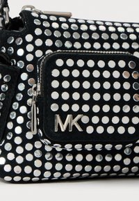 Schwarze Handtasche mit silbernen metallischen Punkten, ausgestattet mit einem Reißverschlußfach und einem geprägten "MK"-Logo. Das Material scheint weich zu sein, mit einer strukturierten Oberfläche.