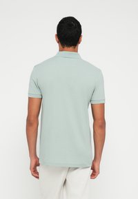 Svetlozelené polo tričko s krátkymi rukávmi, klasickým golierom a hladkou textúrou, zobrazené zozadu na bielom pozadí.