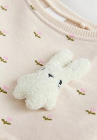 Hellrosa Pullover mit floralem Stickmuster, ausgestattet mit einer flauschigen weißen Hasenapplikation mit schwarzen gestickten Augen und einer strukturierten Oberfläche.