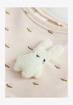 Šviesiai rožinė megztinis su gėlių siuvinėjimu, puikiai papildytas pūkuotu baltu triušiuko aplikė, turinčiu juodai siuvinėjamas akis ir tekstūrinį paviršių.