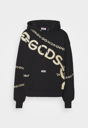 Musta huppari, jossa valkoinen "GCDS" -logo ja ketjumalli, yhdistettynä mustiin nahkahousuihin ja valkoisiin tennareihin. Sujuvat tekstit, rento istuvuus.