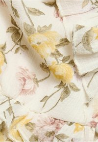 Blommönstrad tyg i krämfärg med volanger. Har gula och rosa rosor med gröna blad, i ett strukturerat lättviktsmaterial.