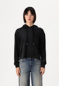Sudadera corta negra con una textura suave, que cuenta con capucha y cordones. Combinada con jeans claros desgastados. Estilo simple y de corte relajado.