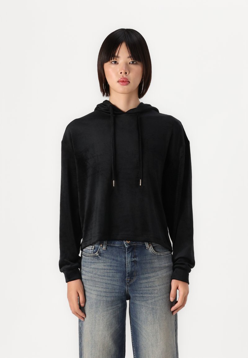 Sudadera corta negra con una textura suave, que cuenta con capucha y cordones. Combinada con jeans claros desgastados. Estilo simple y de corte relajado.