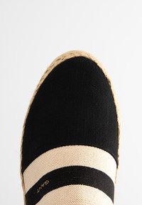 Espadrille noire et beige avec une semelle en jute tressé, dotée d'un capuchon de chaussure noir uni et d'un design rayé beige sur le dessus.