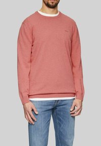 Rosa Baumwoll-Sweatshirt mit langen Ärmeln, Rundhalsausschnitt und gerippten Bündchen; über einem weißen Hemd getragen, kombiniert mit hellblauen Jeans.