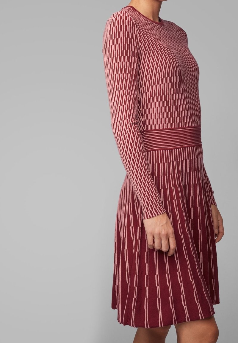 Robe ajustée à manches courtes de couleur bordeaux avec un motif tricoté texturé, présentant une bande horizontale contrastante à la taille et une jupe évasée.