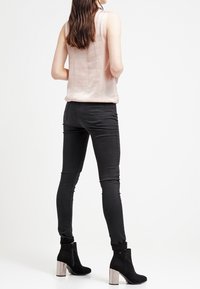 Ljusrosa ärmlös topp, svarta skinny jeans och svarta ankelboots med silverblockklackar, sedd bakifrån. Slät textur, åtsittande design.