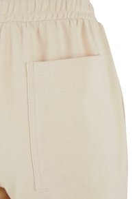 Beige sweatsuitit koostuu teksturoidusta kankaasta, joustavasta vyötäröstä ja yhdestä takataskusta. Suunnittelu on yksinkertaista ja toiminnallista.