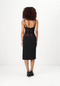 Μαύρο μίντι φόρεμα με διαφανές τούλινο μπούστο και ρυθμιζόμενους straps, που διαθέτει δομημένο σχέδιο και εφαρμοστή σιλουέτα, συνδυασμένο με μαύρα τακούνια.