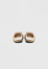 Brown suede slip-on shoes with a soft interior lining, flat black soles, and open backs, featuring a simple and minimalist design.