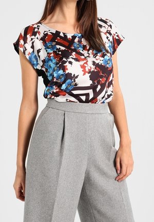 Blusa con estampado floral en blanco, rojo y azul, de tela suave. Combinada con pantalones de pierna ancha de talle alto, en gris claro y con textura.