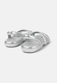 Metallic silver sandals with curved straps and a contoured footbed. The sole features embossed branding, providing a modern design.
