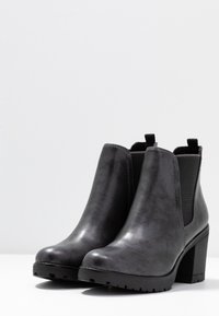 Černé kožené kotníkové boty s hladkým povrchem, elastickými bočními panely a robustním blokovým podpatkem; gumová podrážka s texturovaným gripovým vzorem.