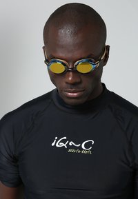 Swimming goggles with blue and gold accents, yellow lenses, and a black swim shirt featuring white and yellow text. Smooth texture, athletic fit.