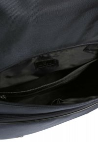 Interno dello zaino in tessuto navy, caratterizzato da una fodera in tessuto liscio, scomparti con zip e un'etichetta del marchio con un logo discreto.