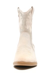 Botas de tobillo de ante beige con costuras decorativas y acentos de tachuelas, que cuentan con una punta afilada y tiradores a cada lado.